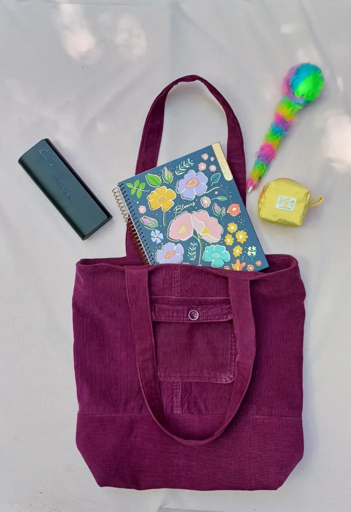 Bolso tote burdeos hecho a mano, acompañado de útiles escolares y accesorios coloridos sobre superficie clara.